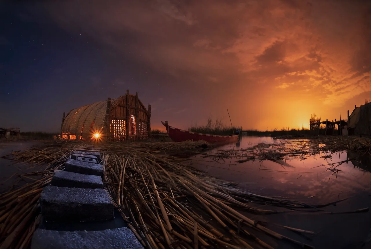 Mesopotamian Marshes of Iraq at night: reed house Mudhif, narrow canoe Mashoof & water.